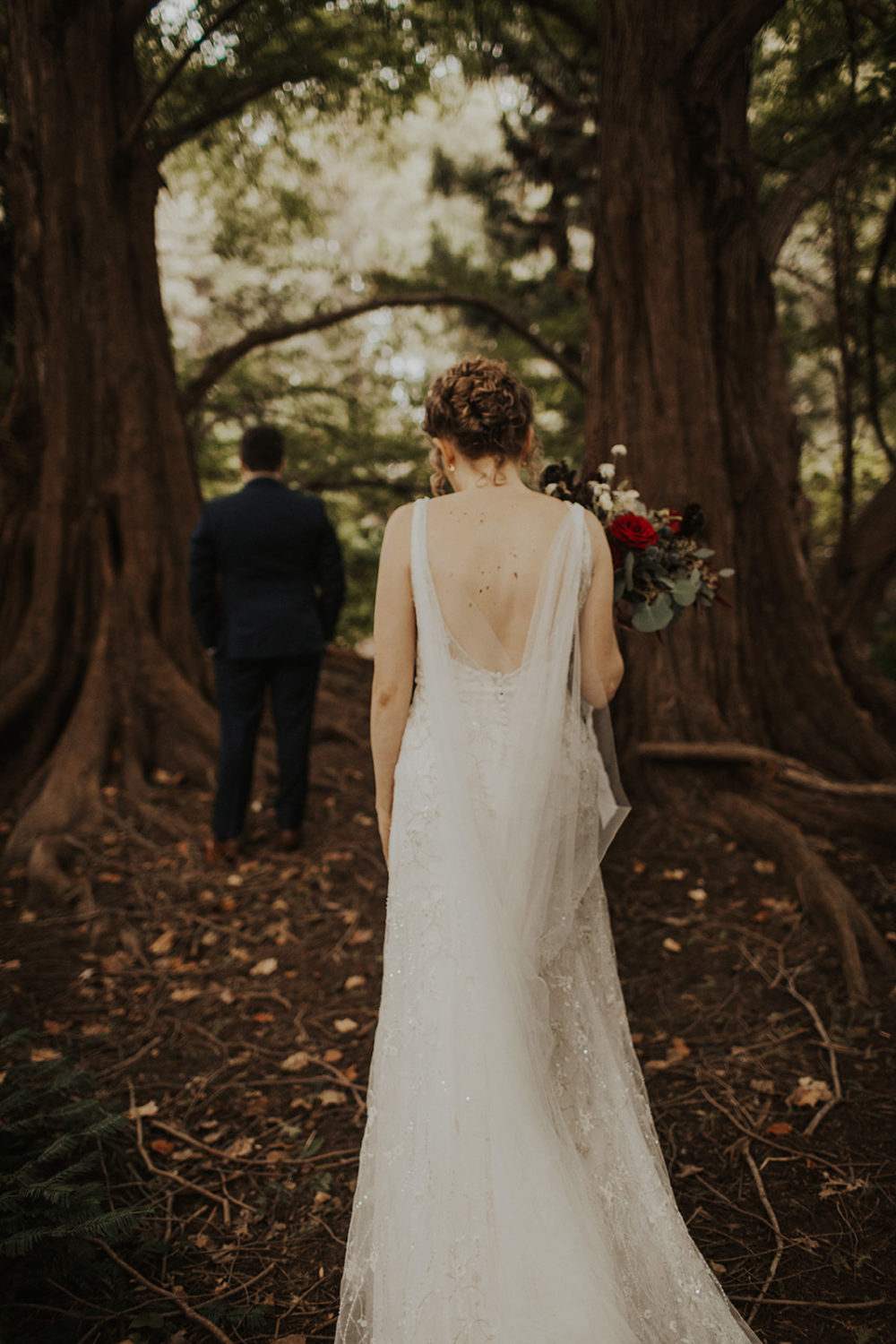 Bride walks through forest holding wedding bouquet for first look