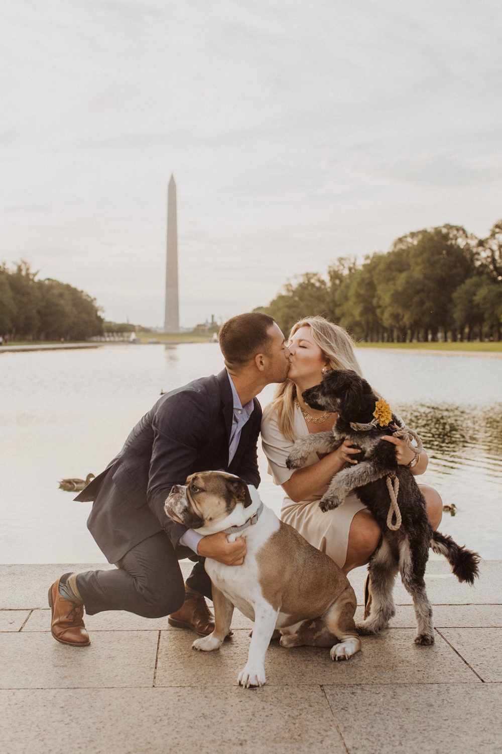 Couple kisses with dogs in front of Lincoln Memorial at sunrise engagement session