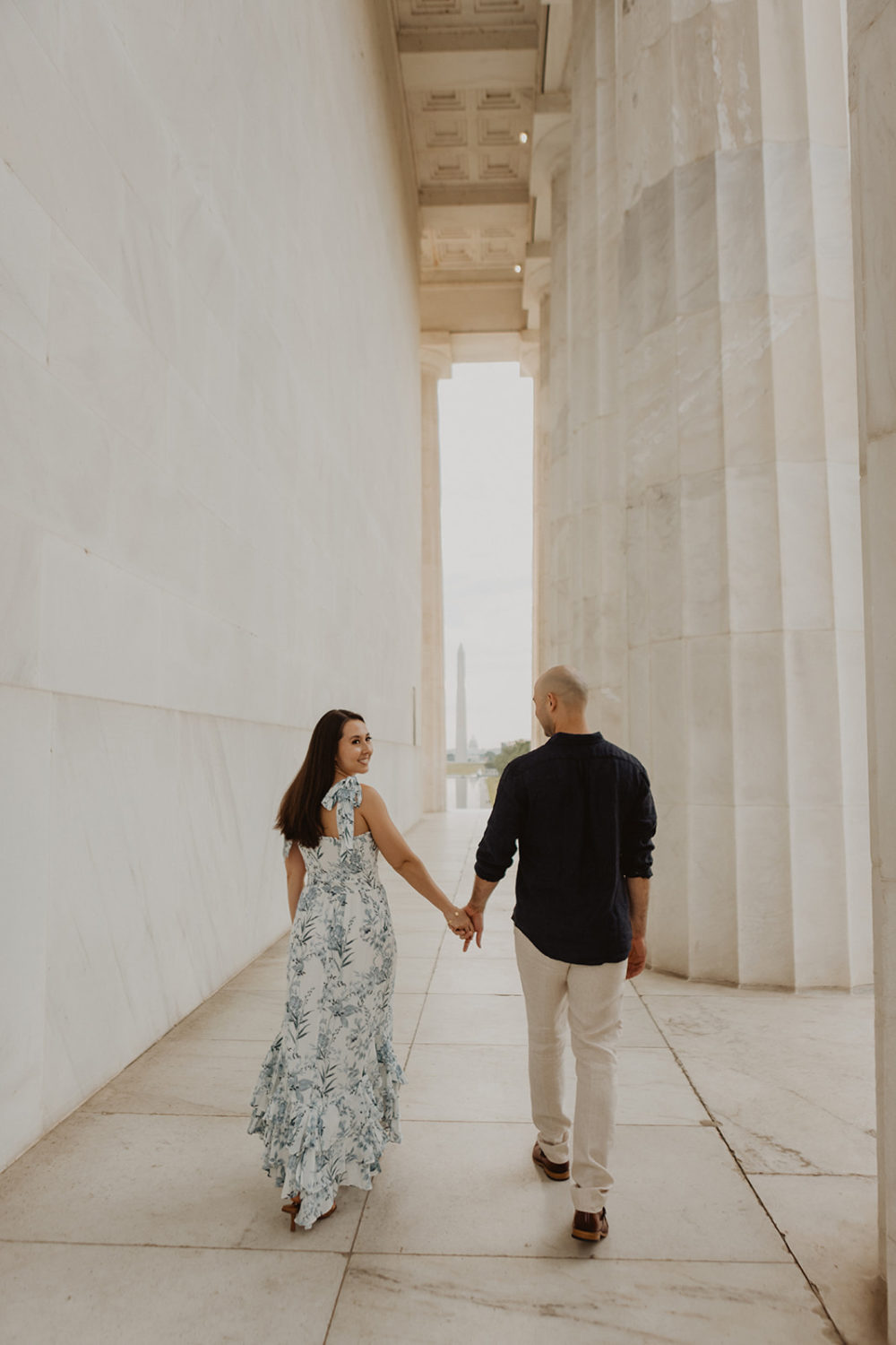 Couple holds hands walking through columns at sunrise engagement session