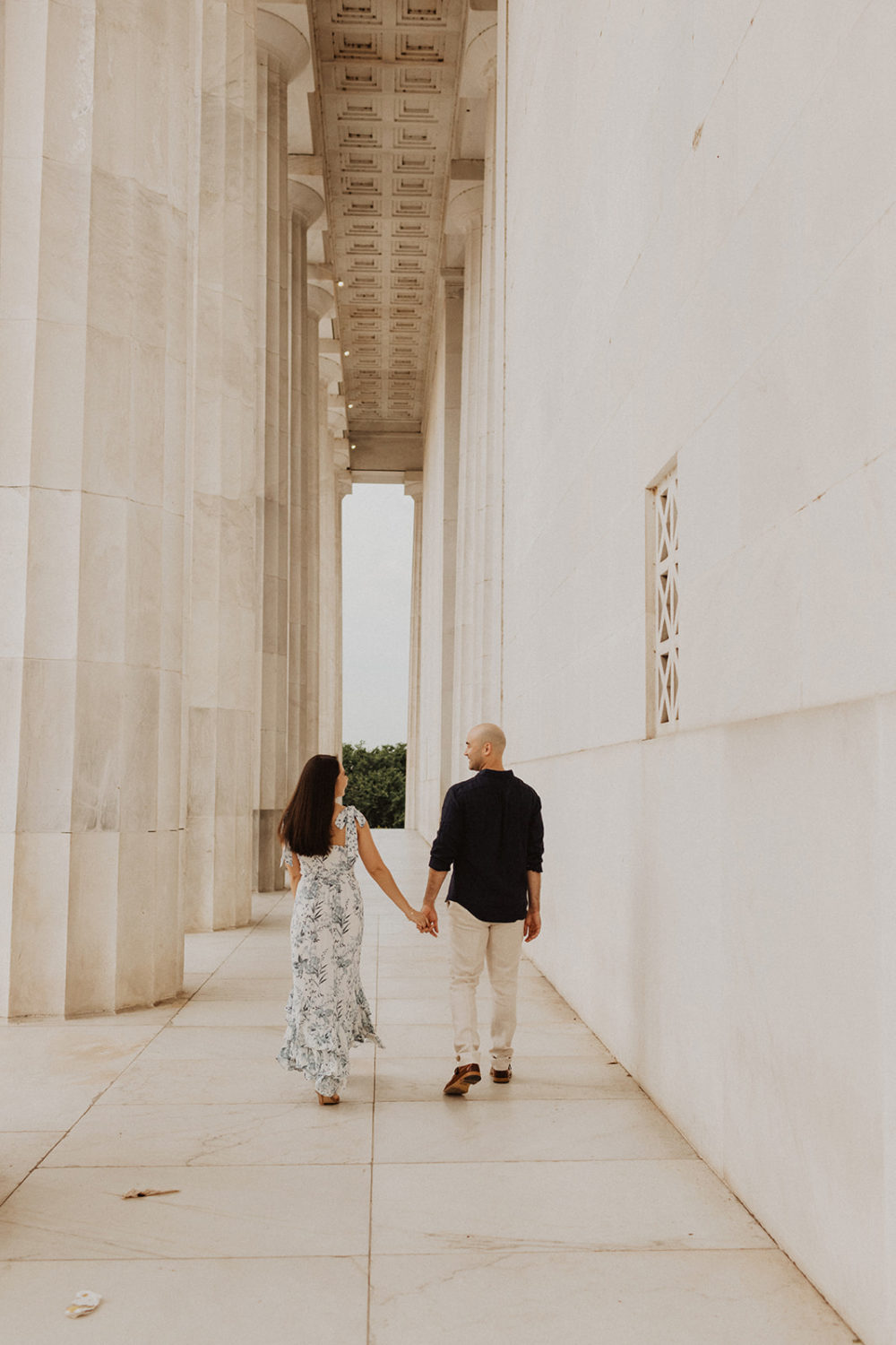 Couple walks along columns at sunrise captured by DC engagement photographer