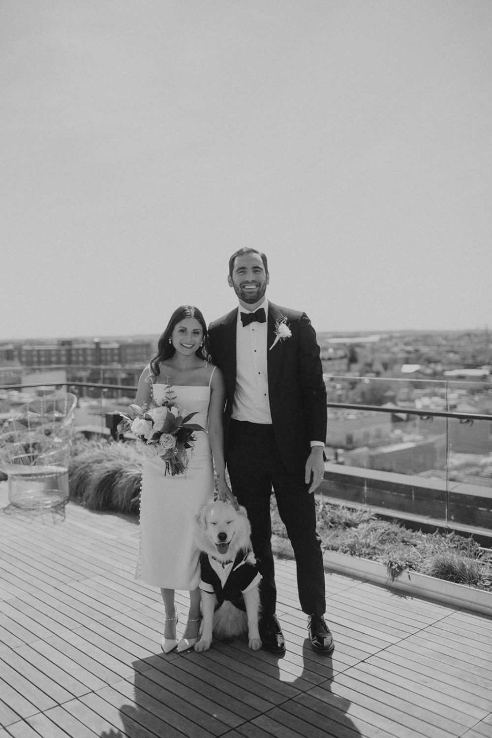 Couple stands with dog wearing tuxedo at DC rooftop elopement 