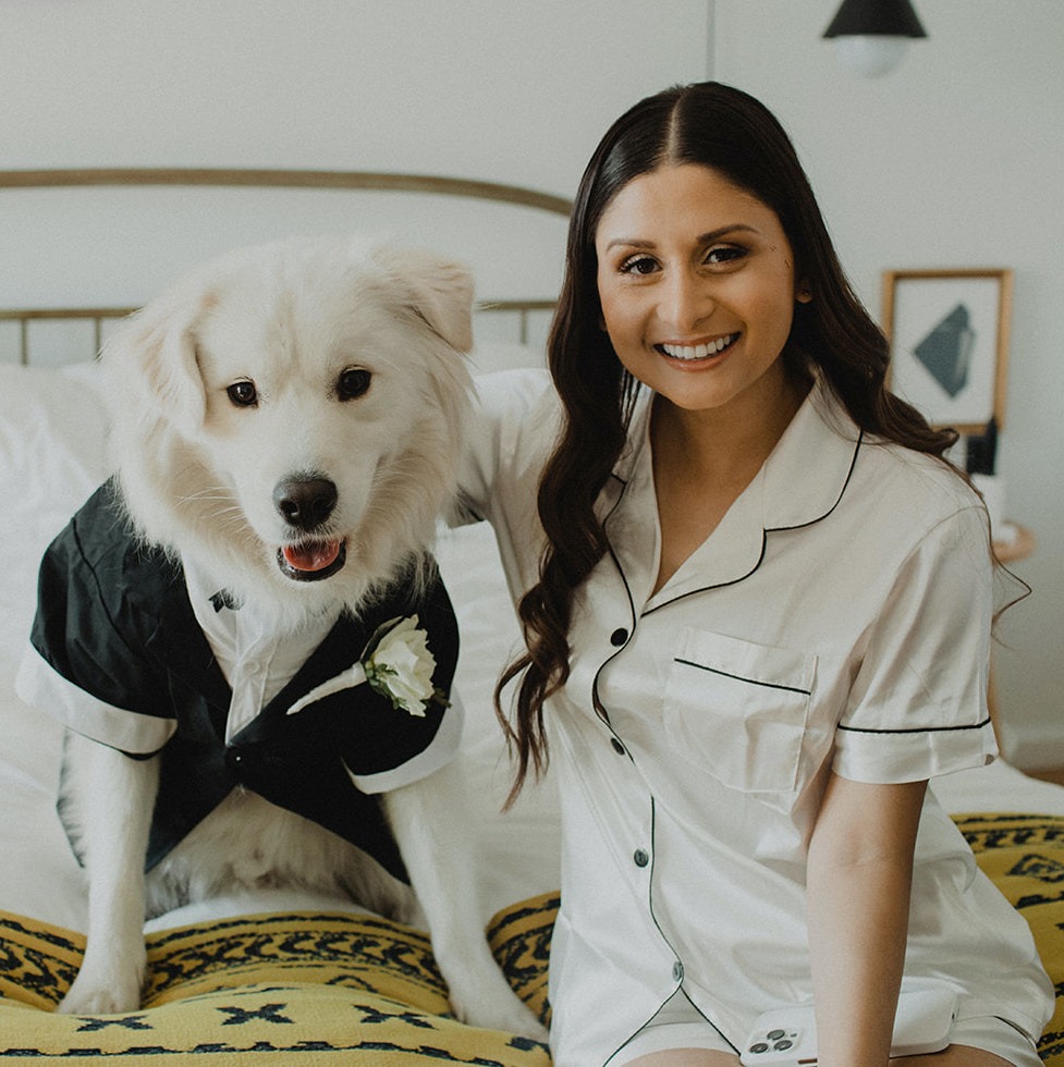 Bride sits in white pajama's with her white dog in a tuxedo