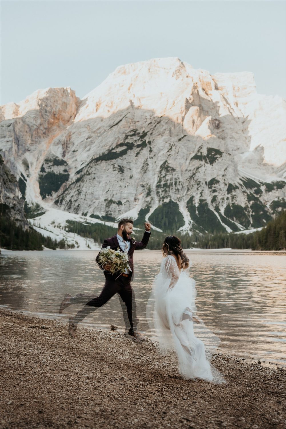Couple jumps by lake at Dolomites elopement captured by destination wedding photographer 
