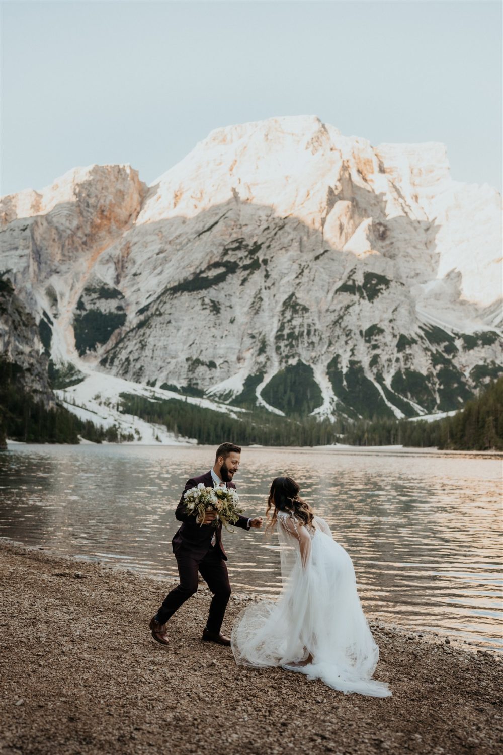 Couple jumps by lake at Dolomites elopement captured by destination wedding photographer 