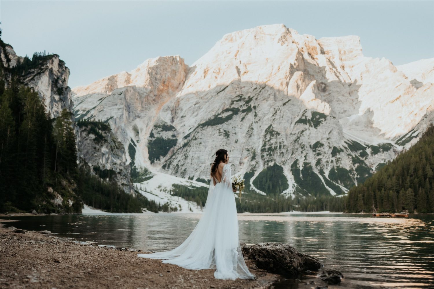 Bride standings holding wedding bouquet lakeside at Dolomites elopement