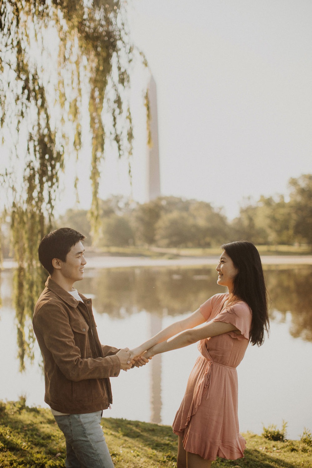 Couple holds hands under tree by reflecting pool at sunrise engagement session