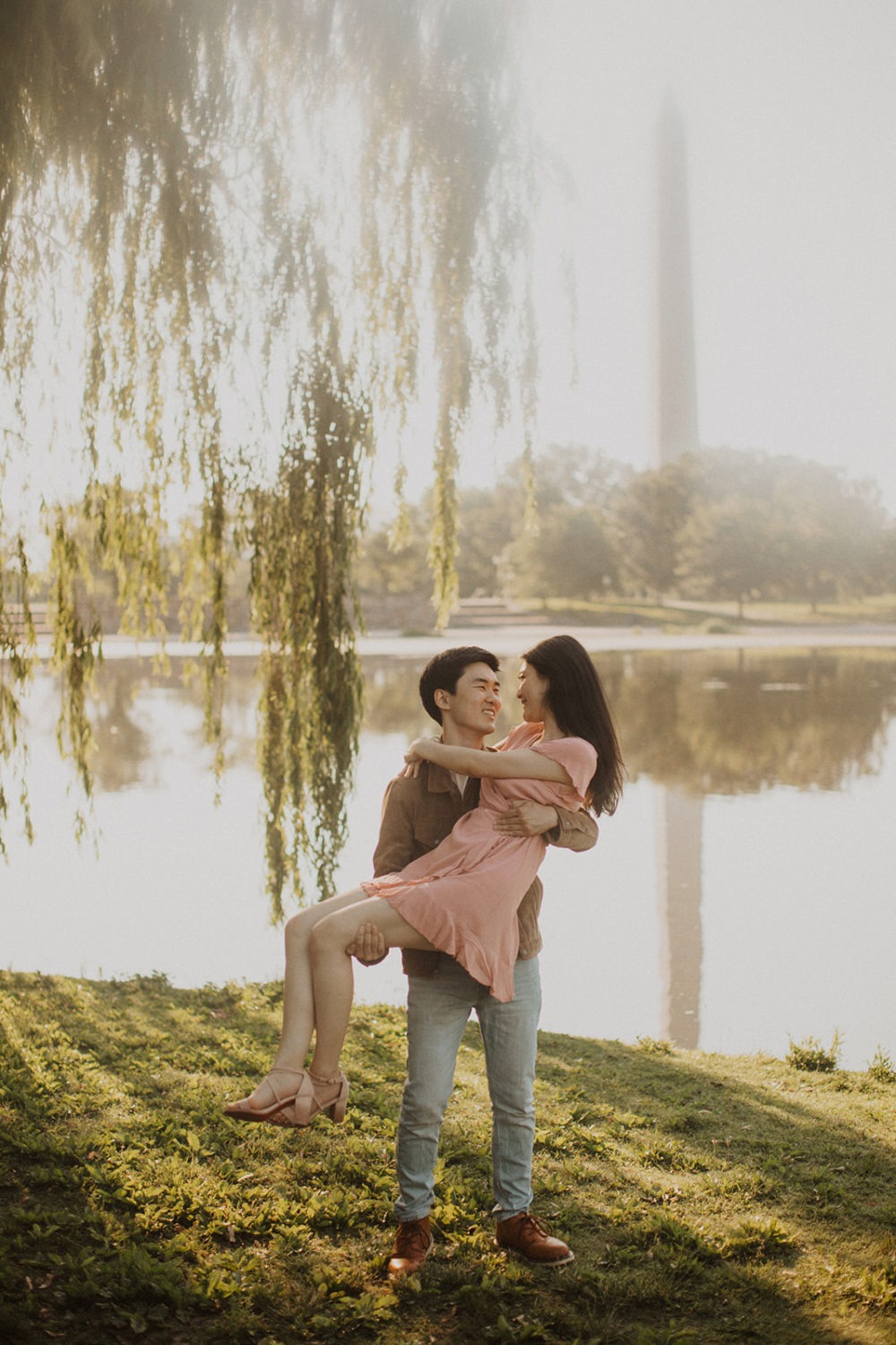 Man carries woman under tree by reflecting pool at sunrise engagement session