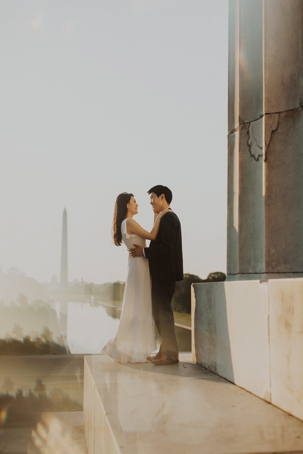 Couple embraces against Lincoln Memorial column at sunrise engagement session