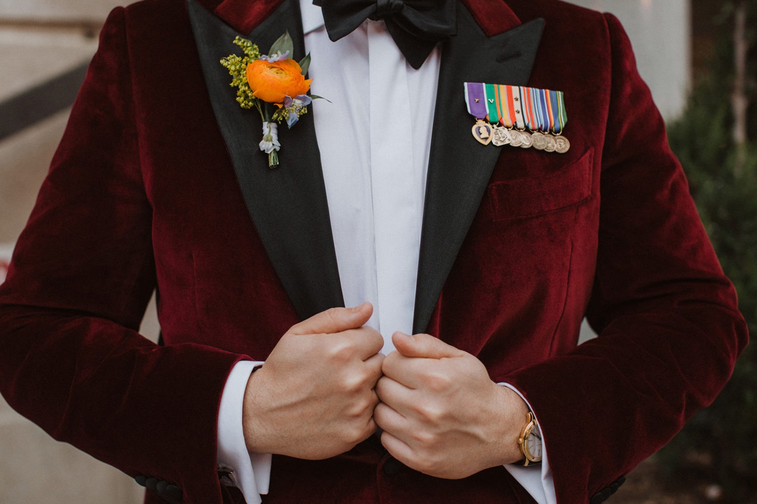 Groom holds suit jacket with boutonierre and medals