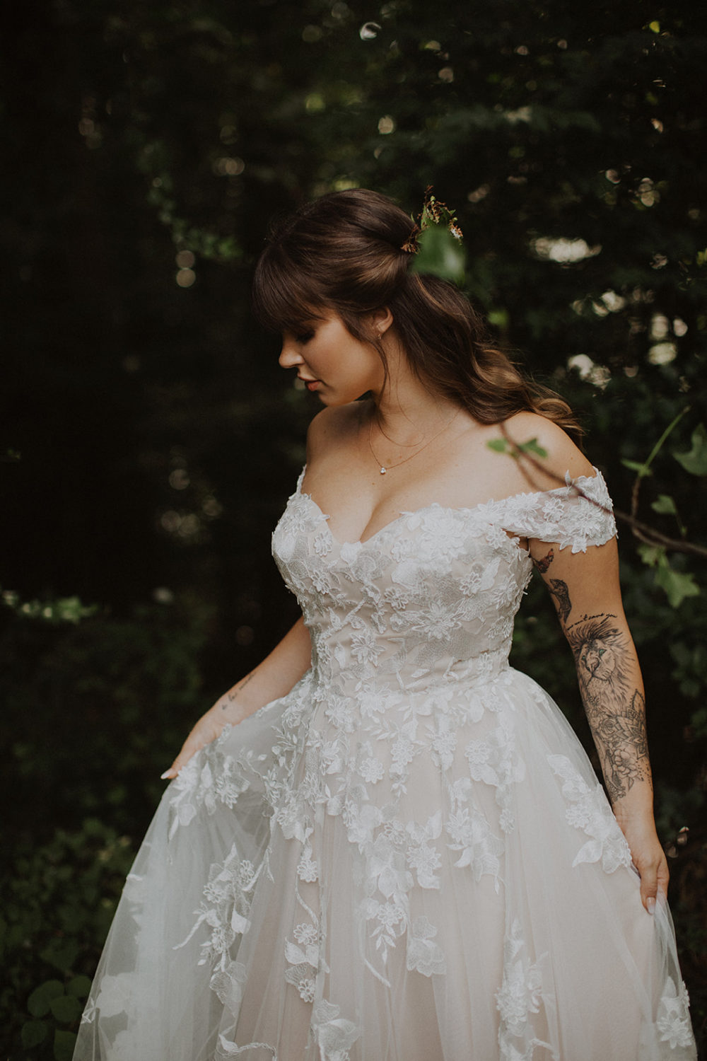 Bride stands holding dress in woods 