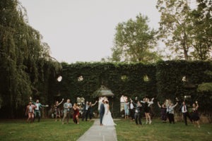 Wedding party jumps and cheers with couple at garden wedding