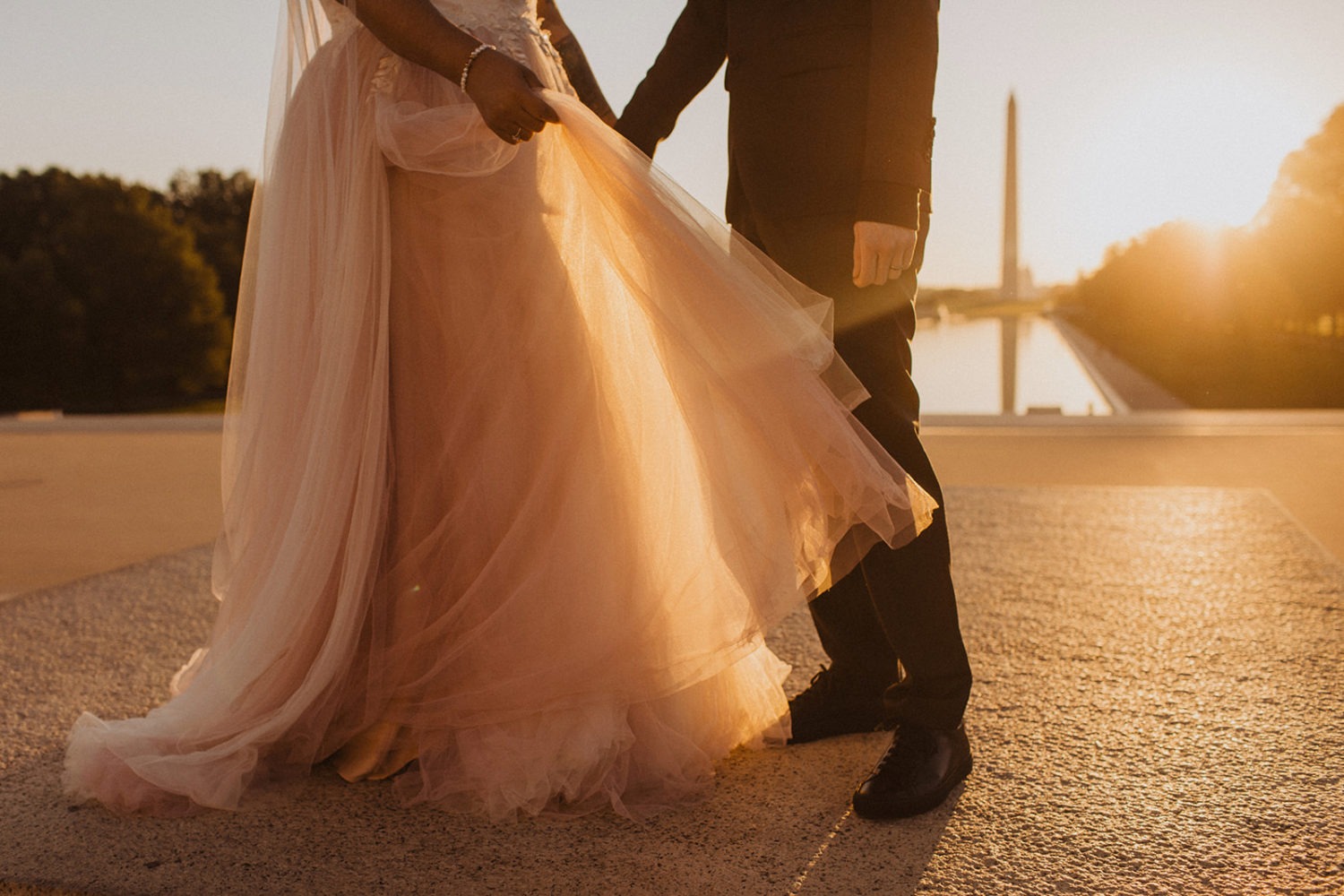Bride holds dress standing beside groom at sunset elopement