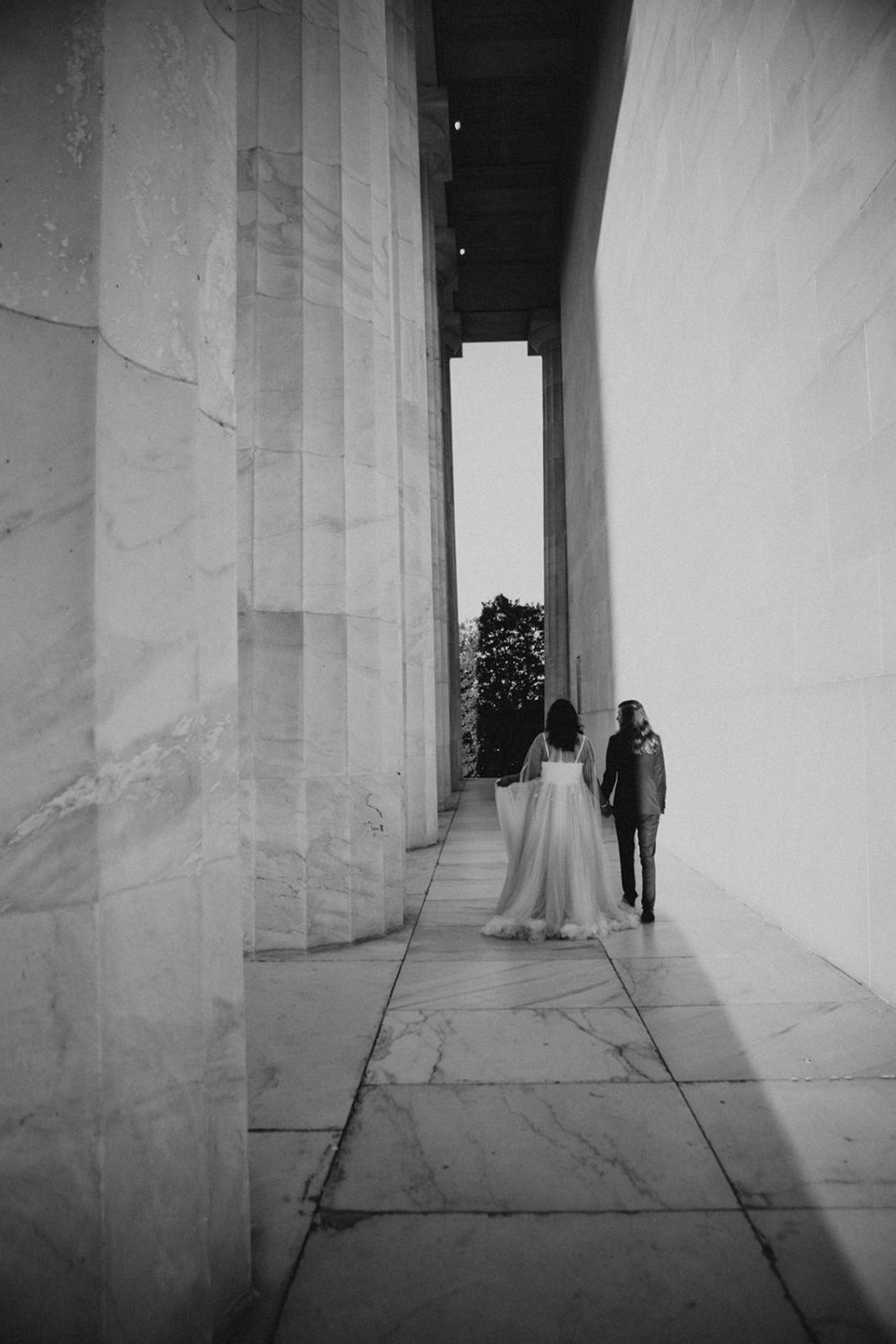 Couple holds hands walking through columns at Lincoln Memorial sunset session