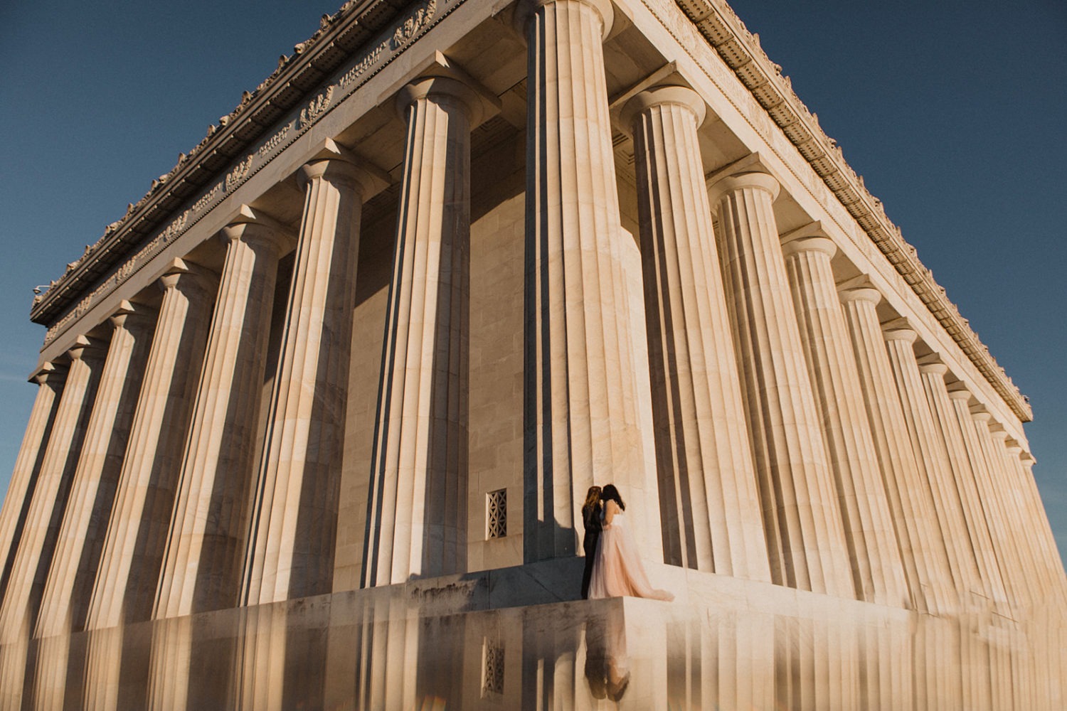 Couple stands beside columns of Lincoln Memorial sunset elopement