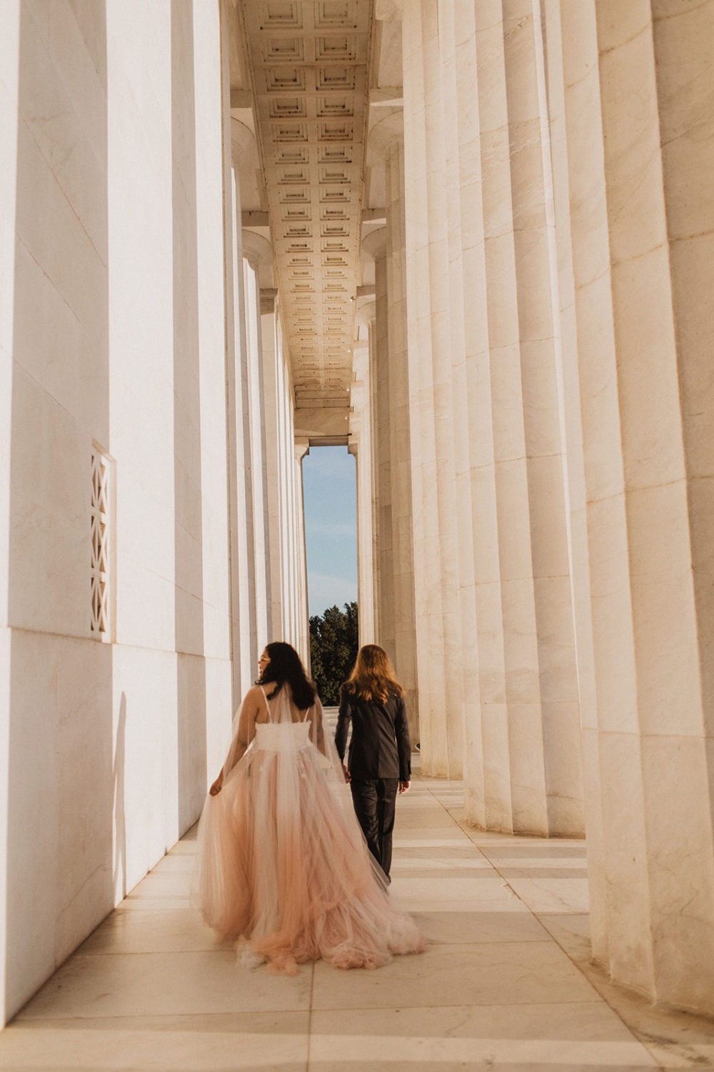 Couple holds hands walking through Lincoln Memorial columns