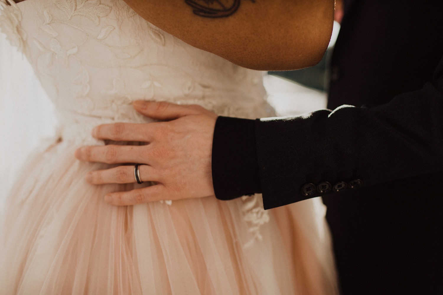 Groom's hand with wedding band holds bride's waist
