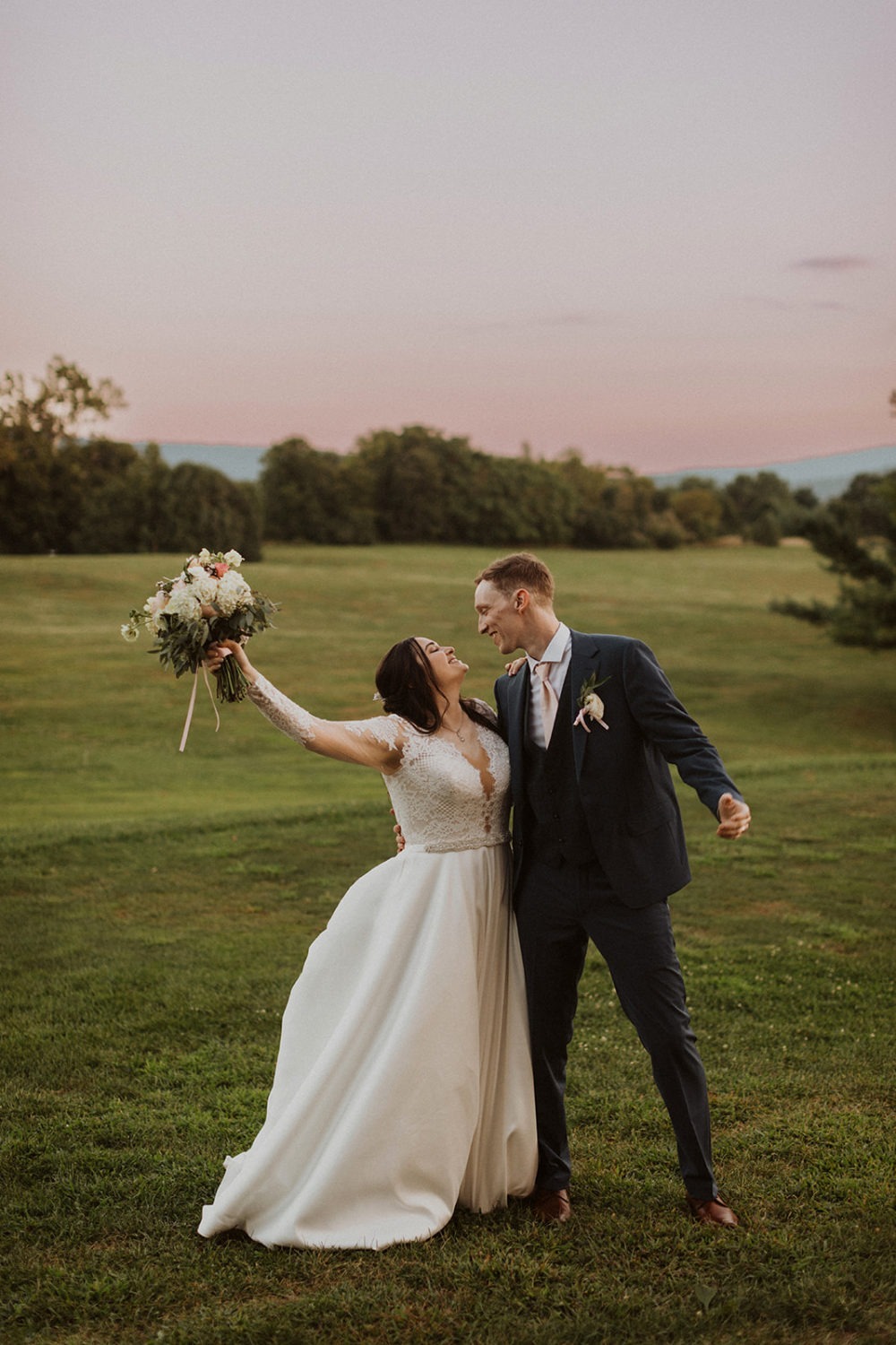 Couple embraces with bouquet in the air at farm sunset wedding