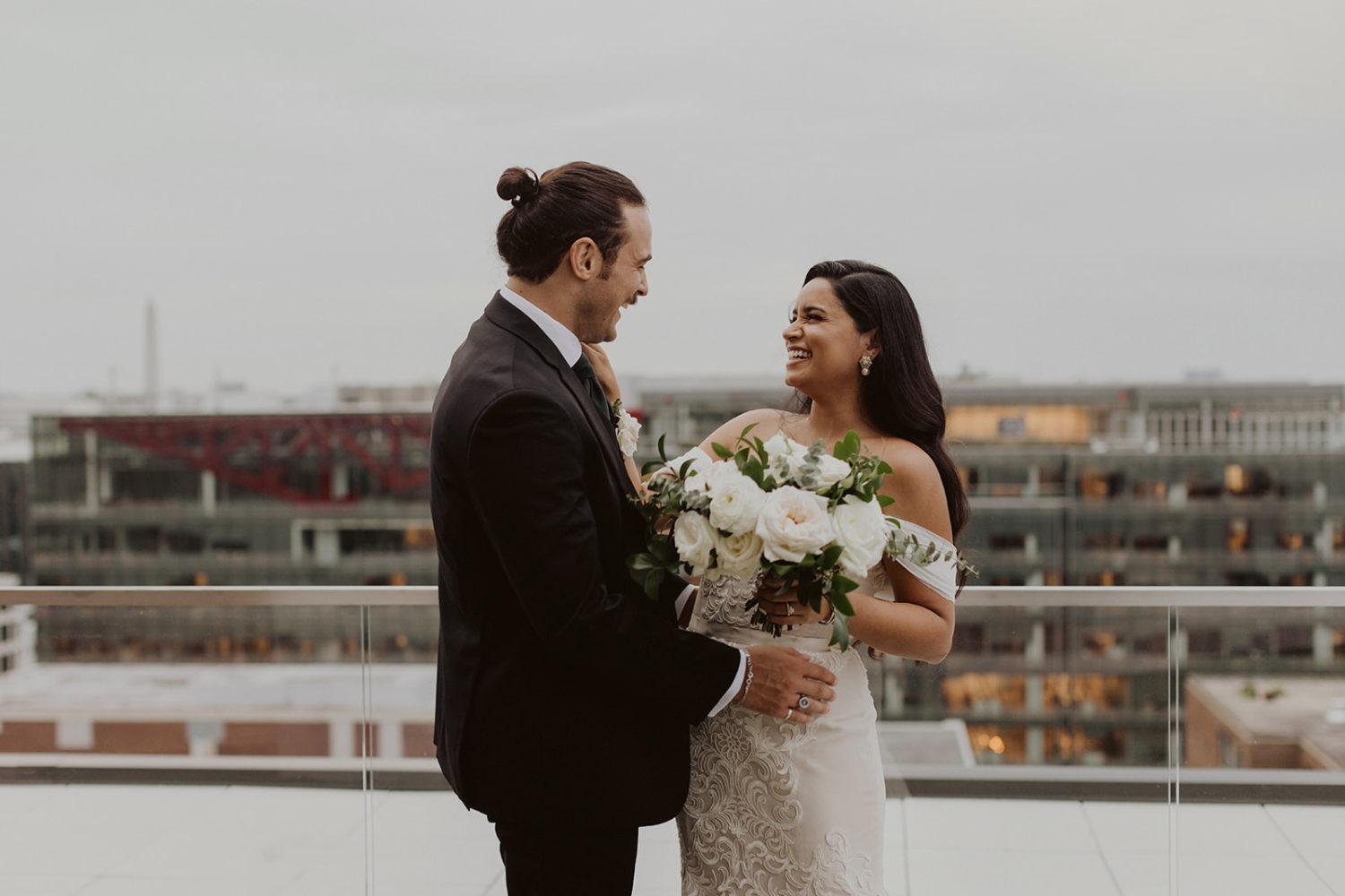 couple laughs while holding white rose bouquet on DC rooftop