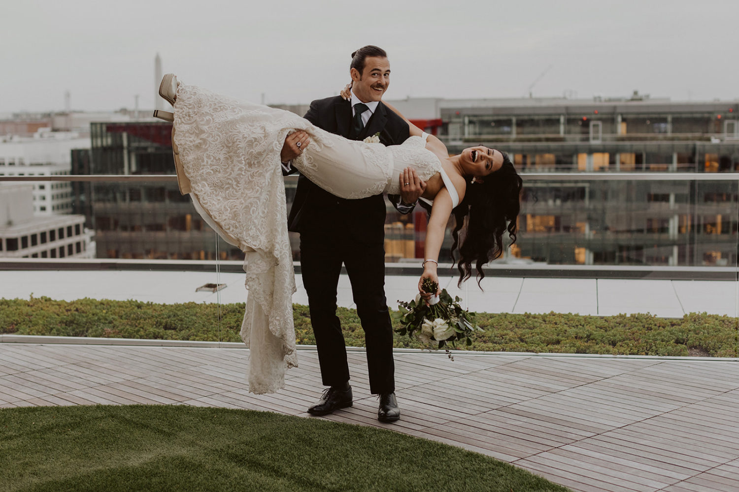 groom holds bride on DC rooftop wedding venue with Washington Monument in background