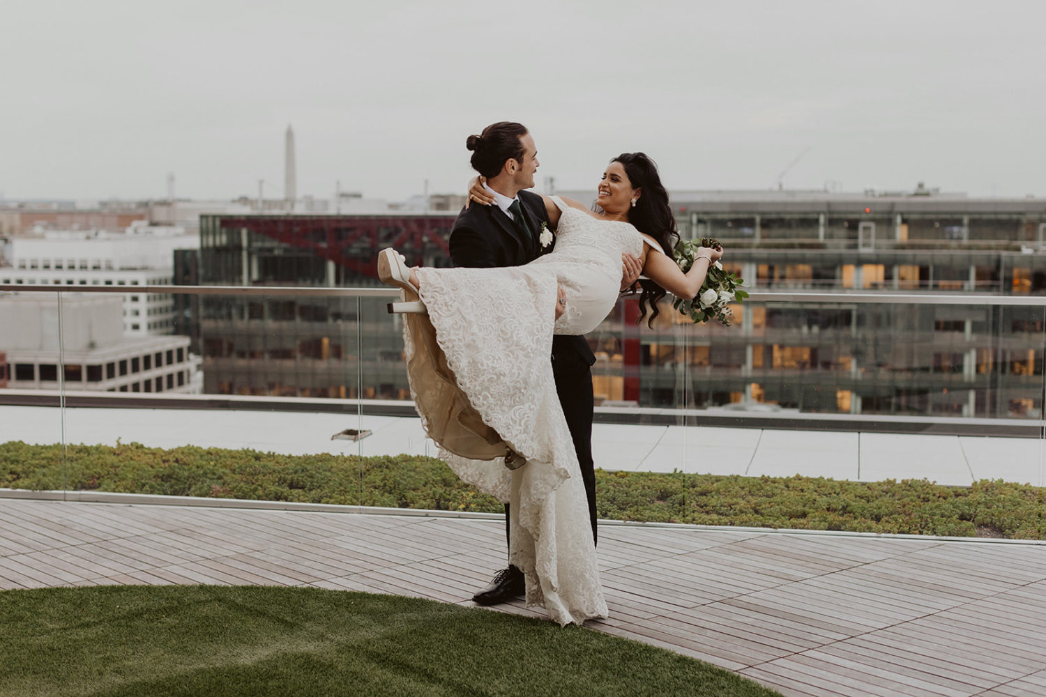 groom carries bride at DC rooftop wedding venue with Washington monument in background