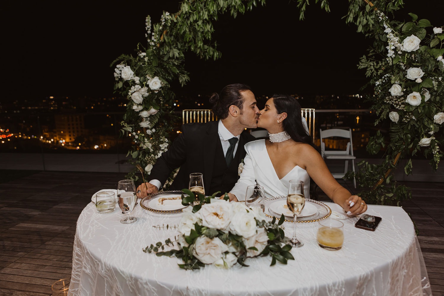 couple kisses at head table with white florals and greenery