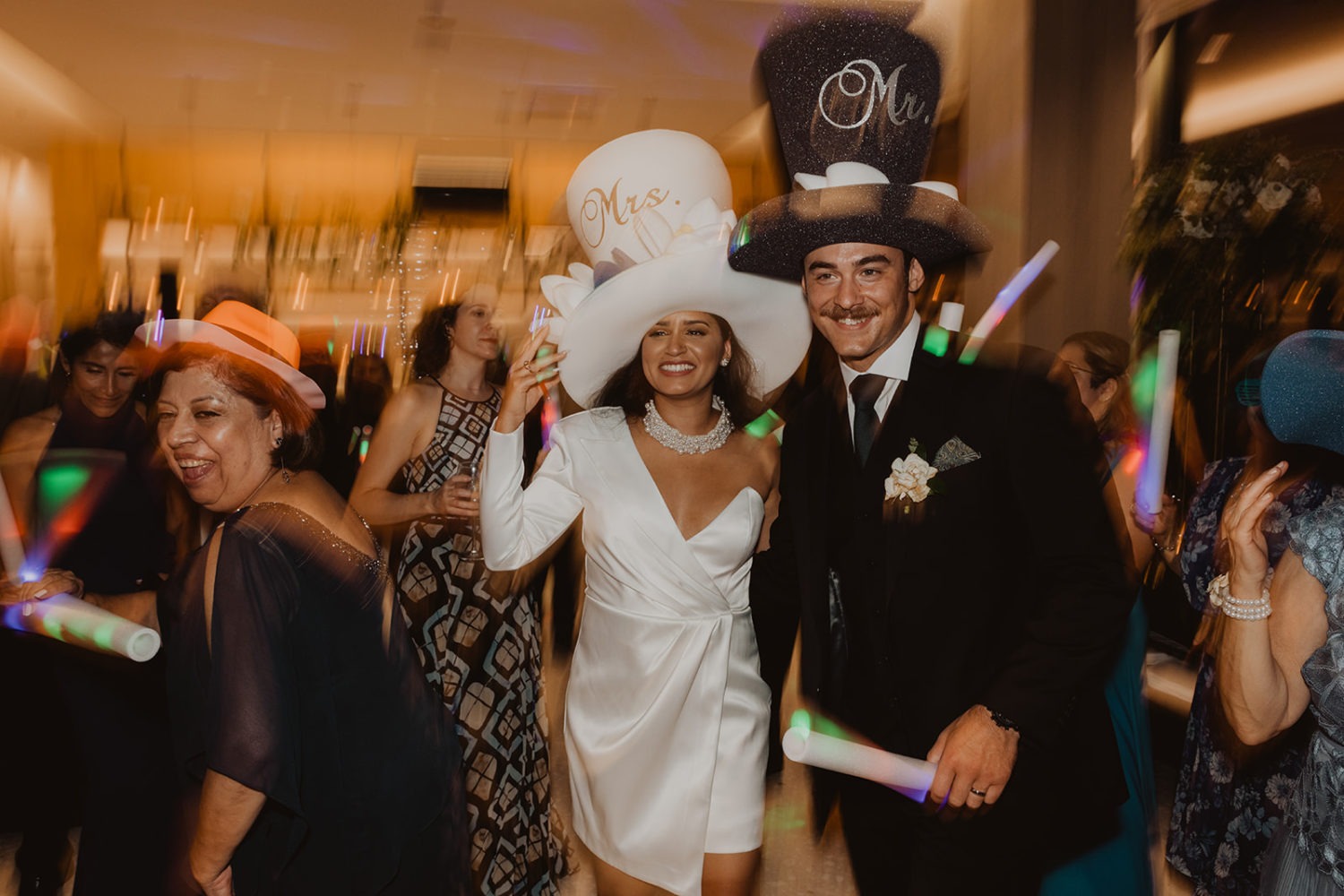 couple dances with glow sticks and large hats at wedding reception dance party