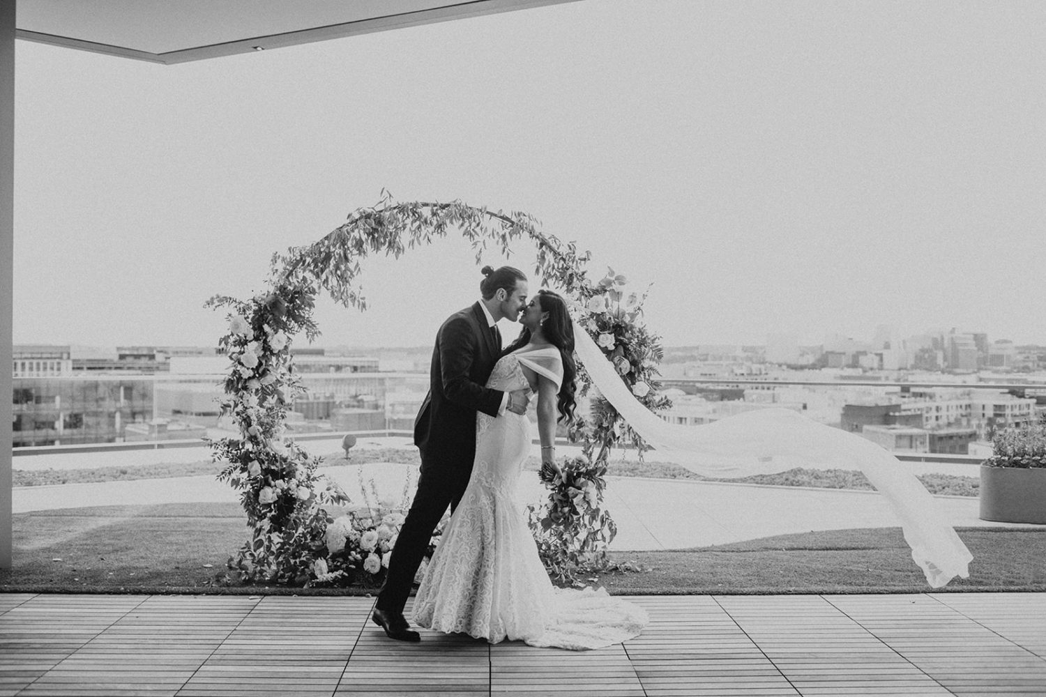 couple kisses on DC rooftop with veil flowing in wind