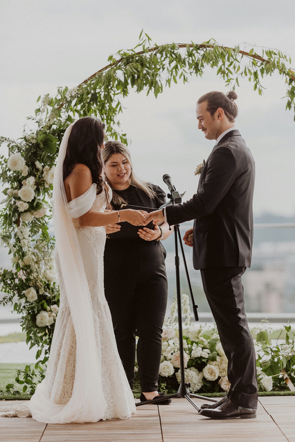 couple exchanges rings under floral arch at DC rooftop wedding