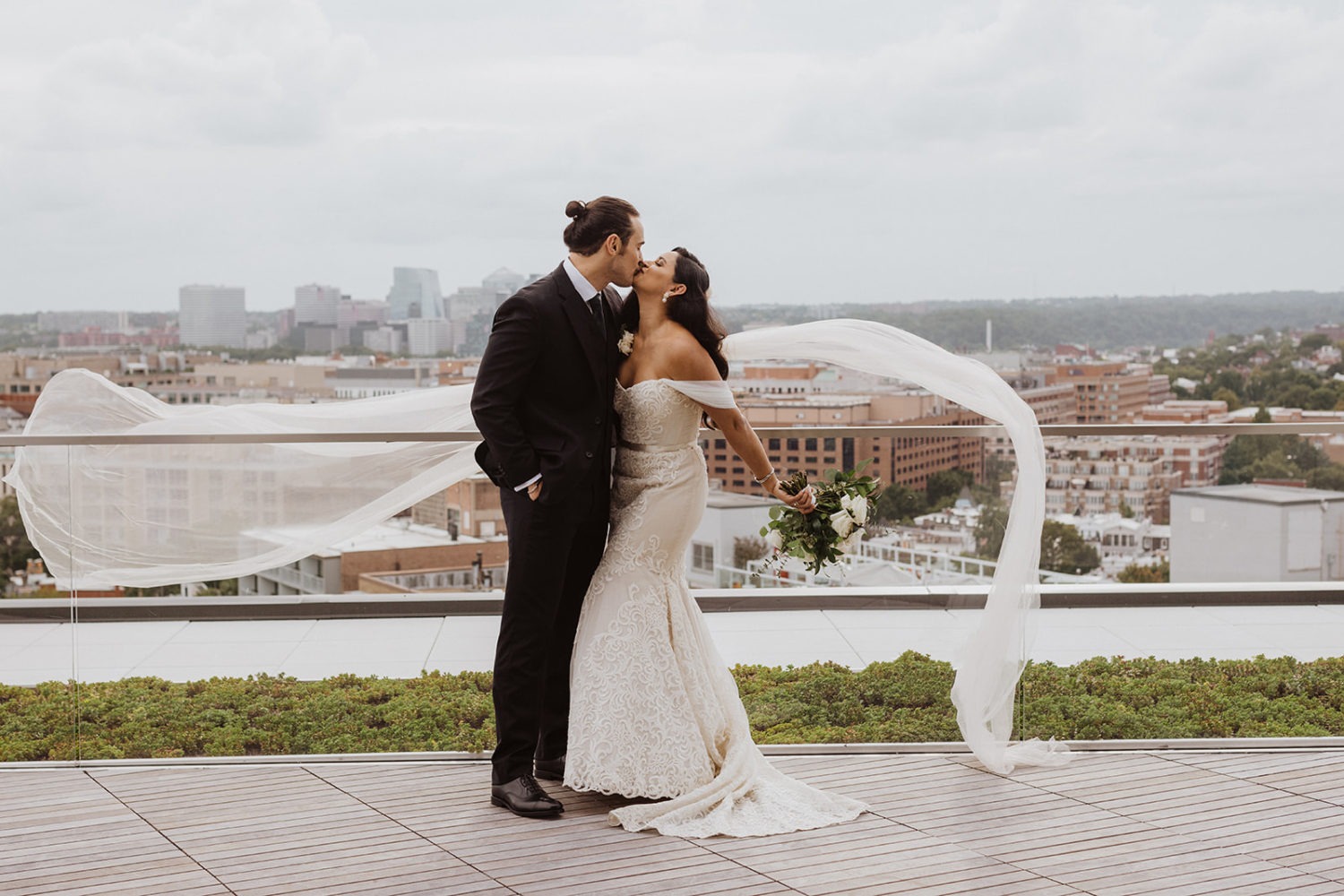 couple kisses on DC rooftop wedding venue with veil flowing in wind