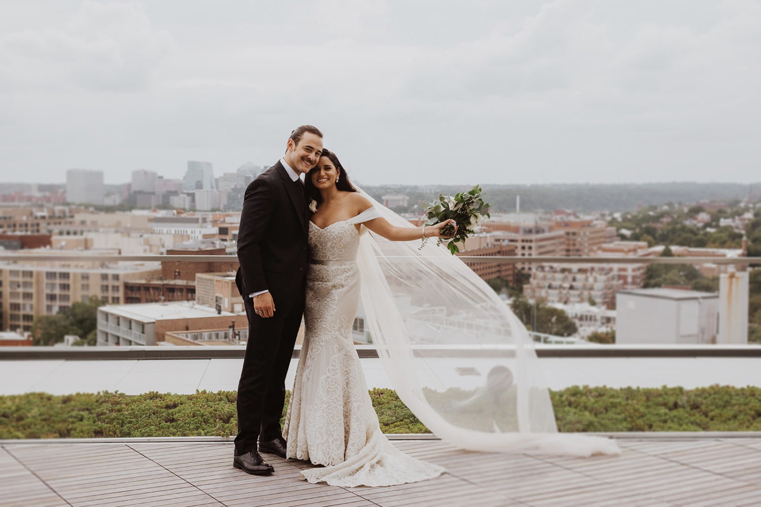 couple embraces with white veil flowing in wind on DC rooftop