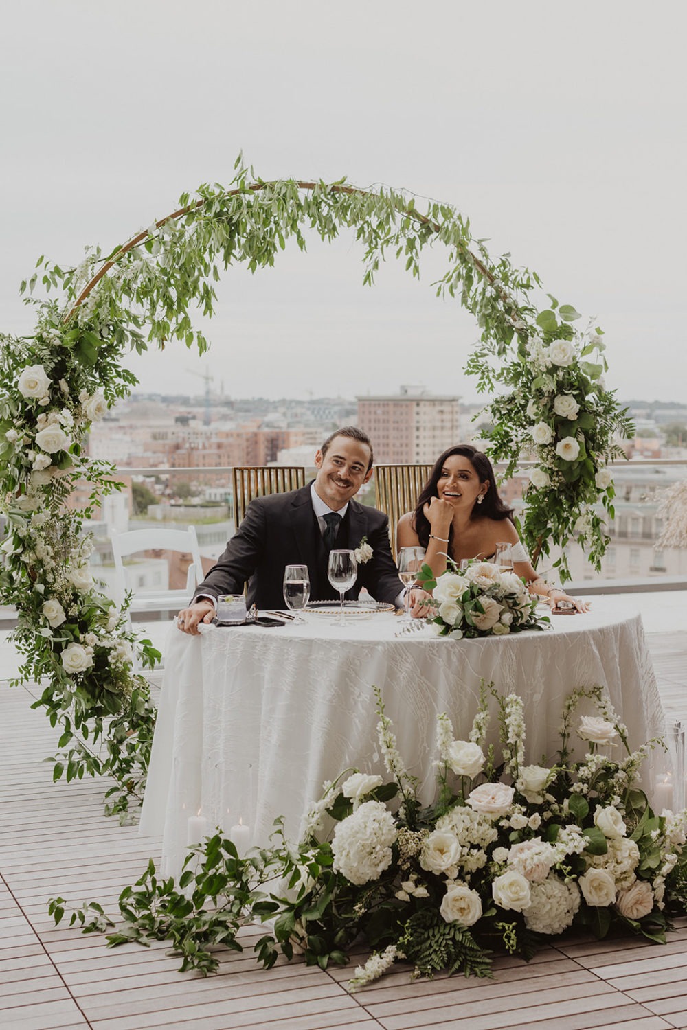 couple kisses at table decorated with white florals at DC rooftop wedding venue