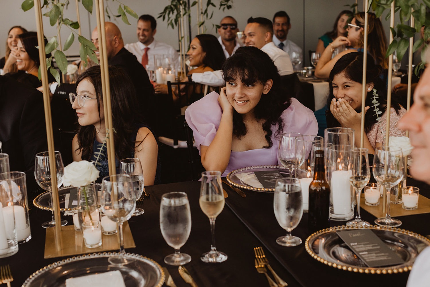 guests laugh seated at gold and black decorated wedding reception table