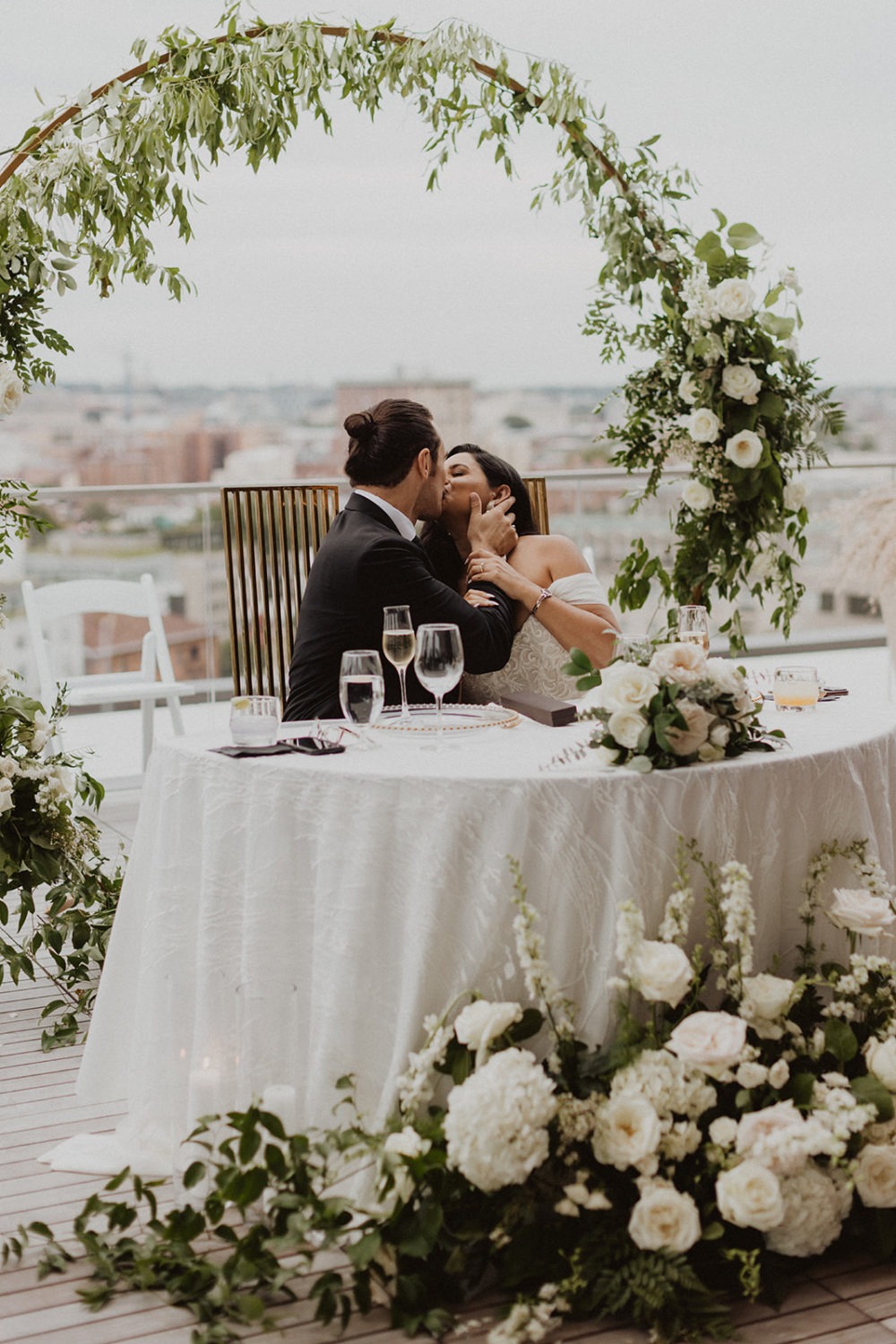 couple sits at table decorated with white florals at DC rooftop wedding venue