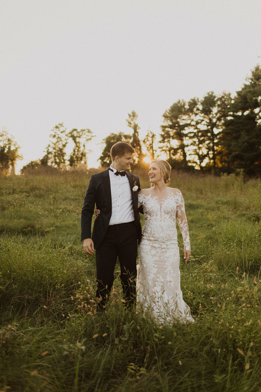 couple walks through field of grass at sunset at Airlie Warrenton, VA wedding venue 
