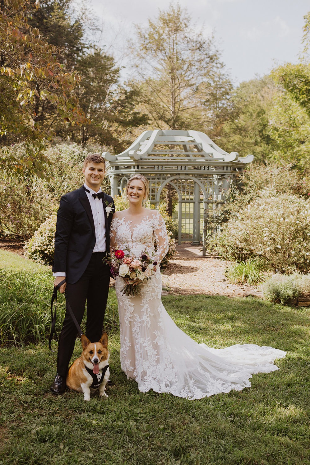 Couple stands with dog wearing tux 