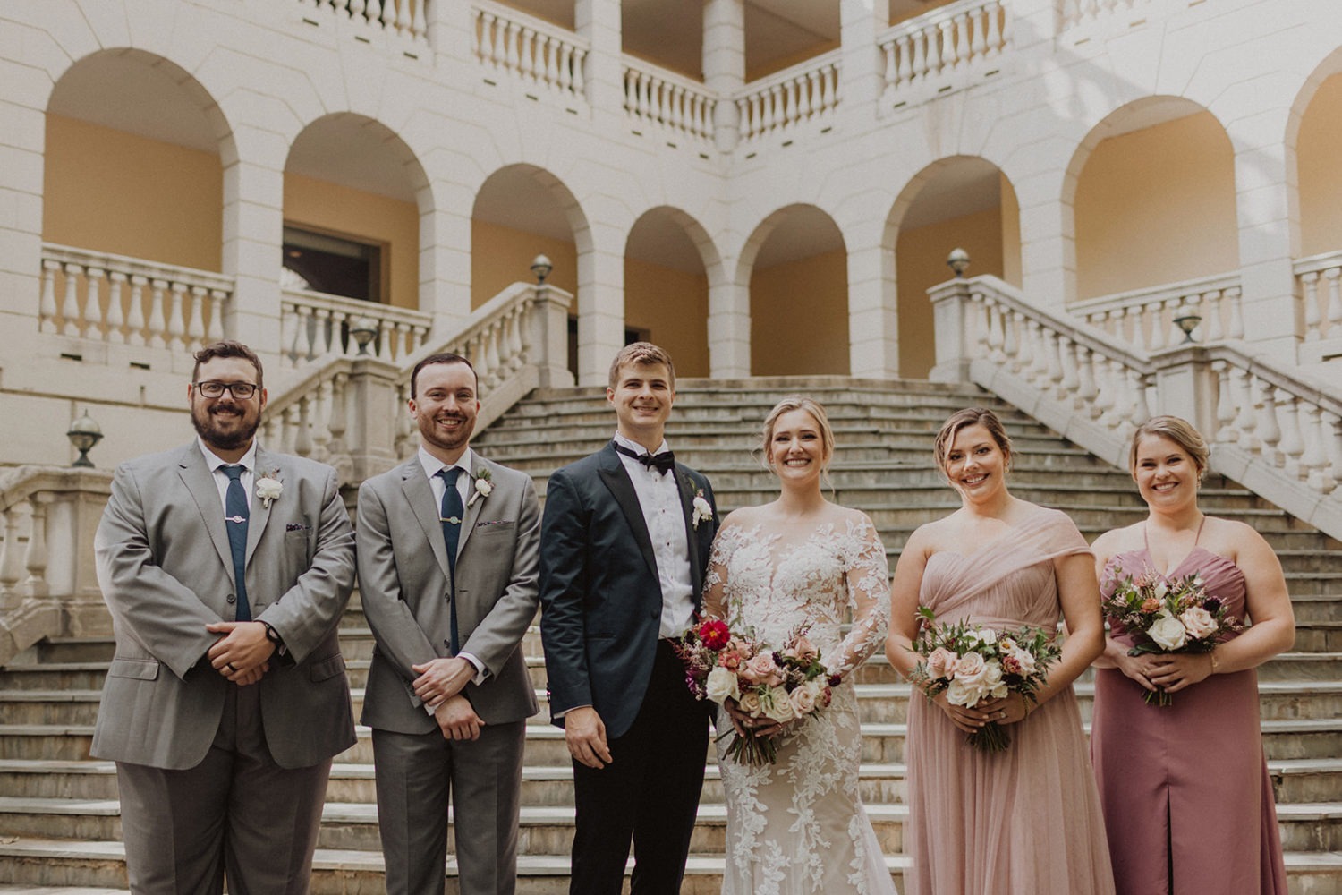 Couple stands with wedding party on grand staircase at Airlie Warrenton, VA wedding venue 