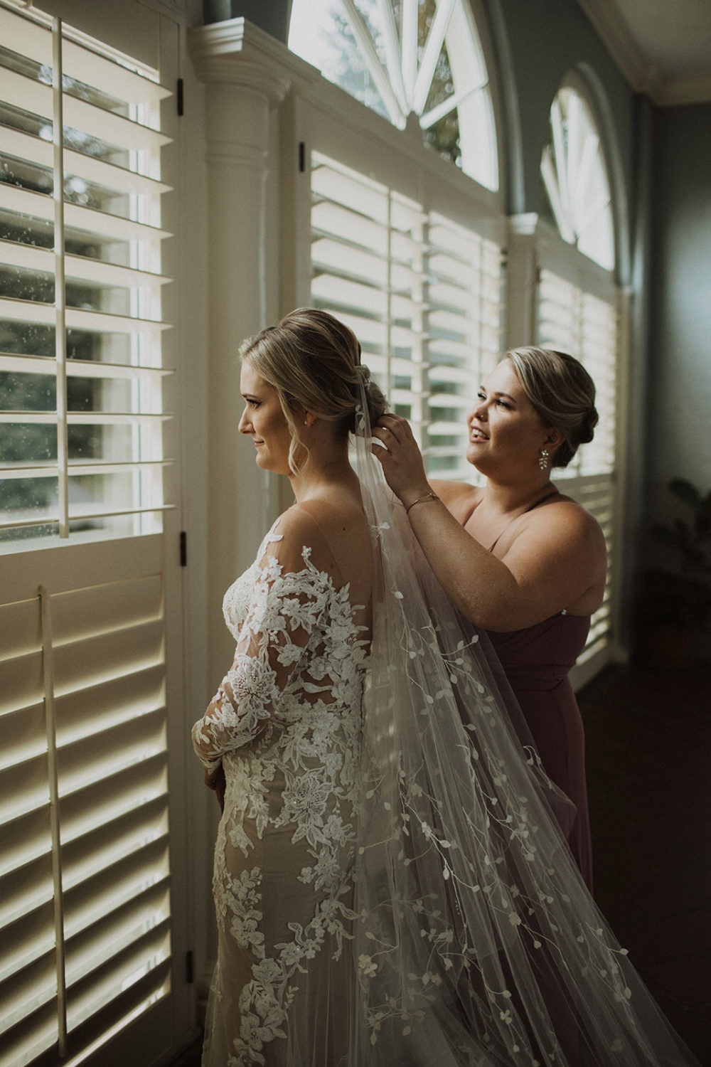bride puts on wedding veil at window 