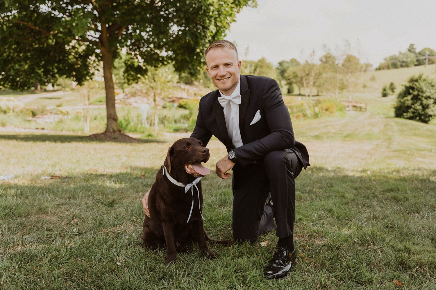 groom holds dog in grassy yard at wedding