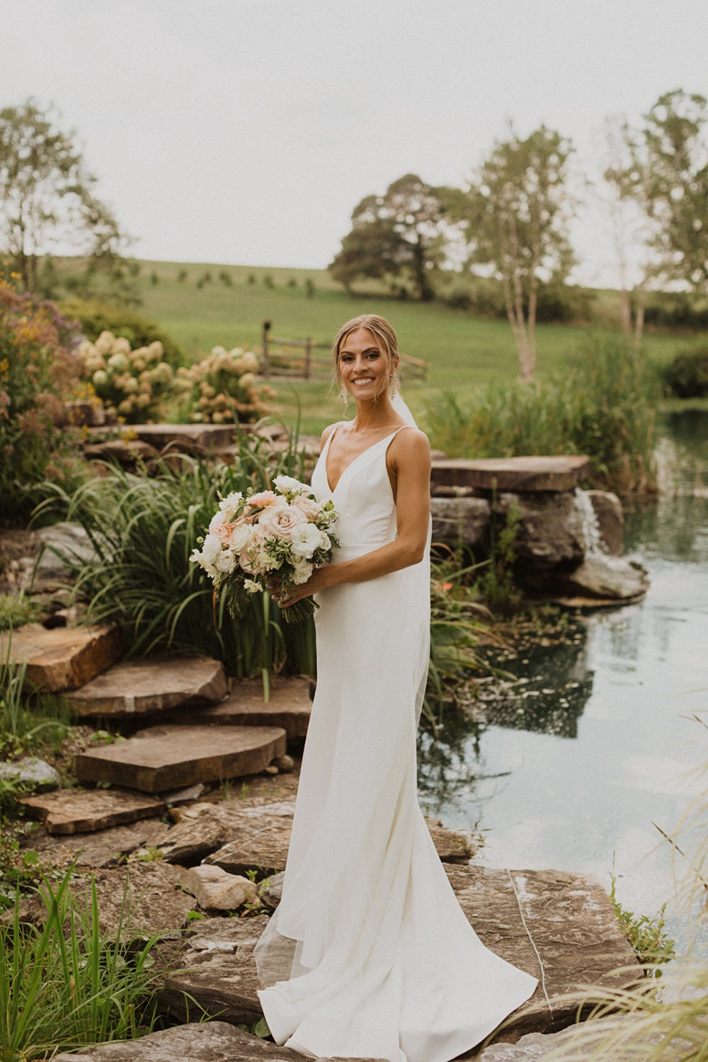 bride holds wedding bouquet beside pond