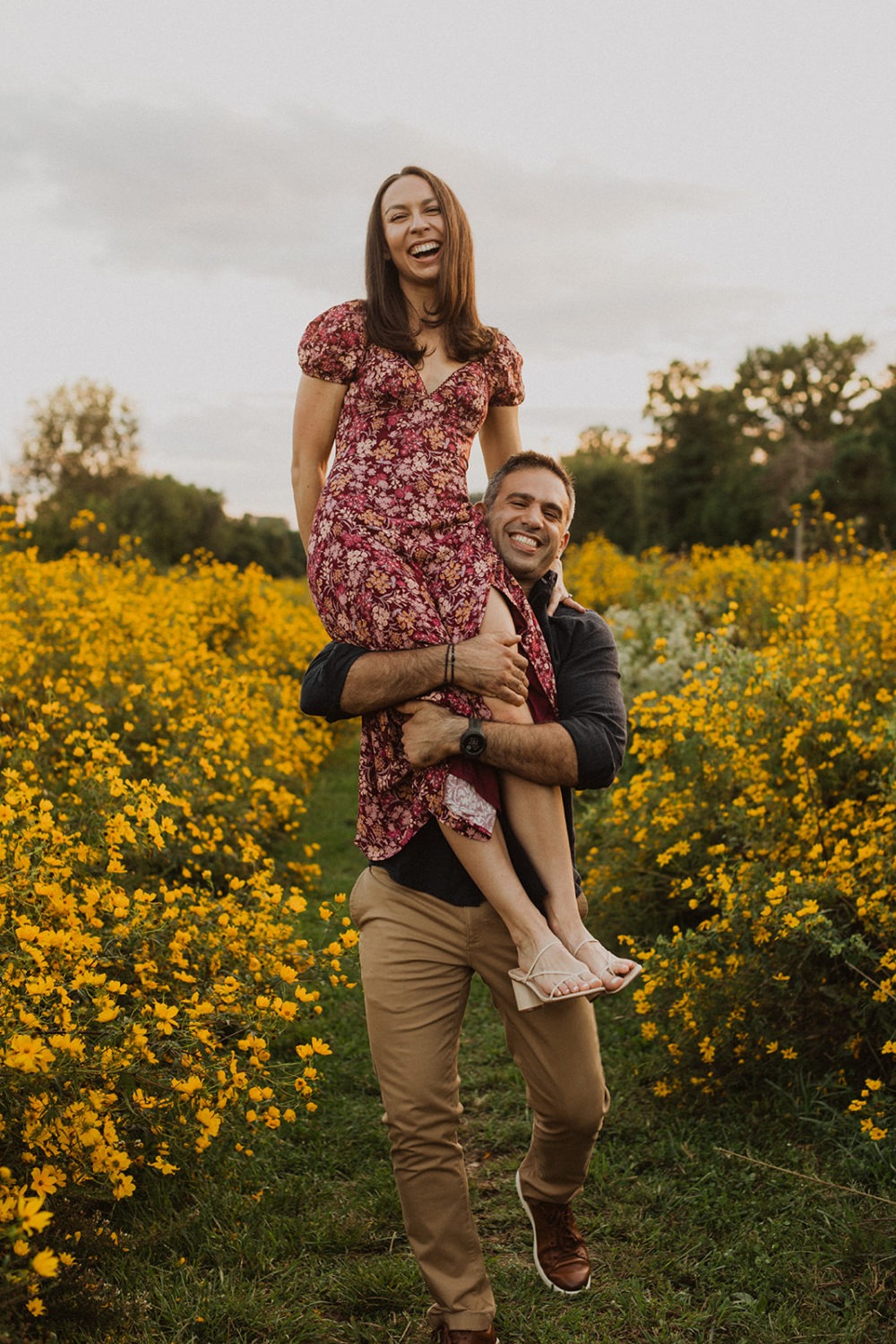 man carries woman through field at wildflower engagement session