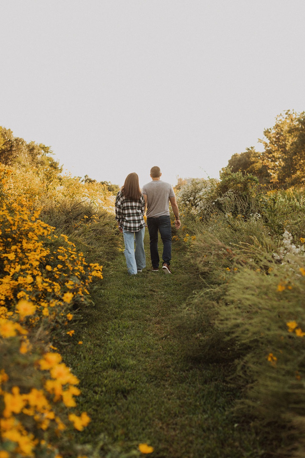 couple walks through wildflower field holding hands at engagement session