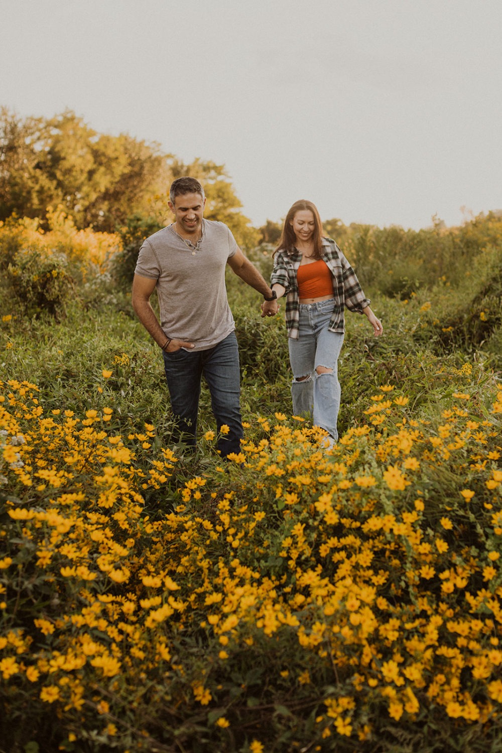 couple walks through wildflower field holding hands at engagement session