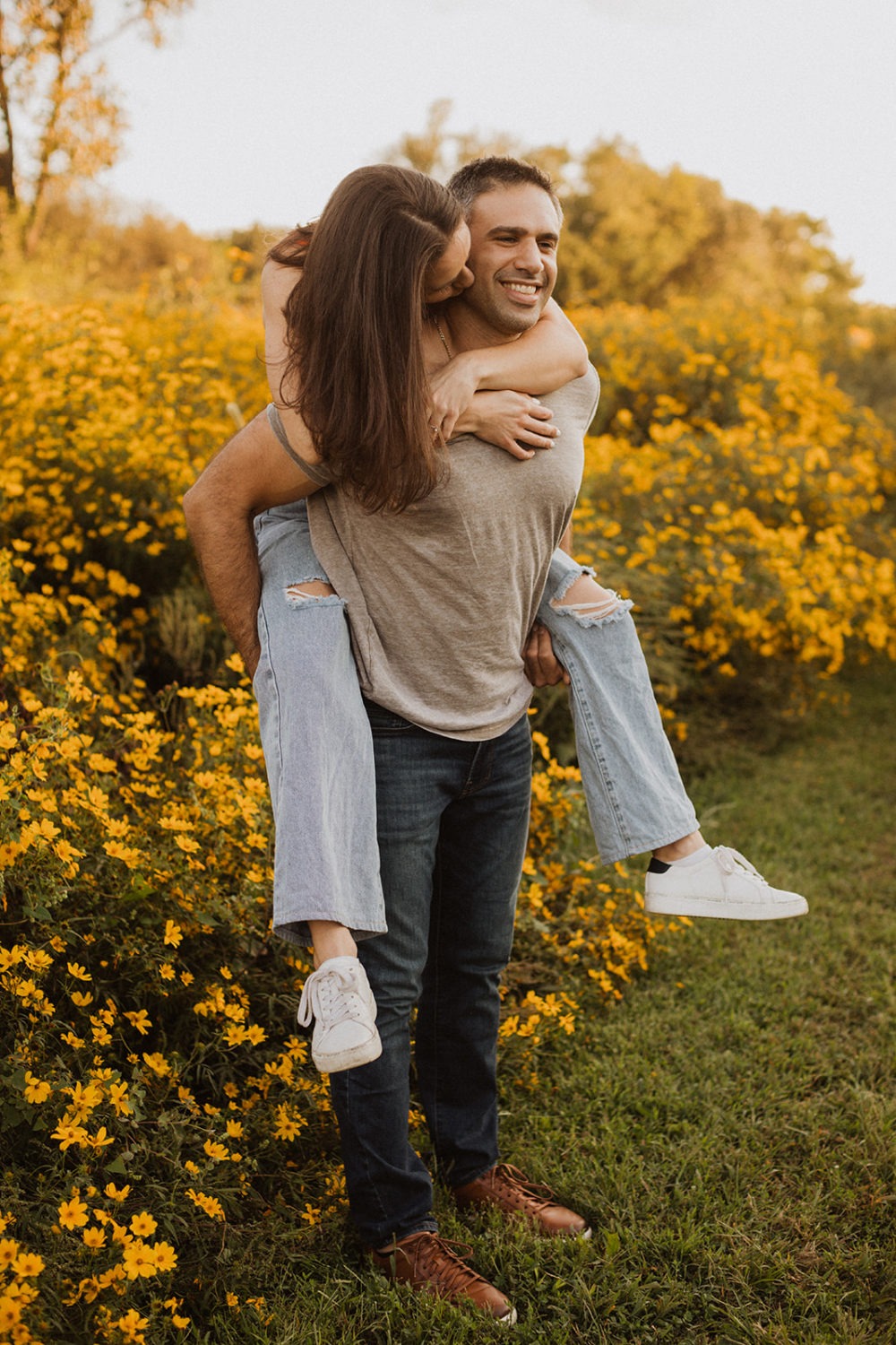 man carries woman through field at wildflower engagement session
