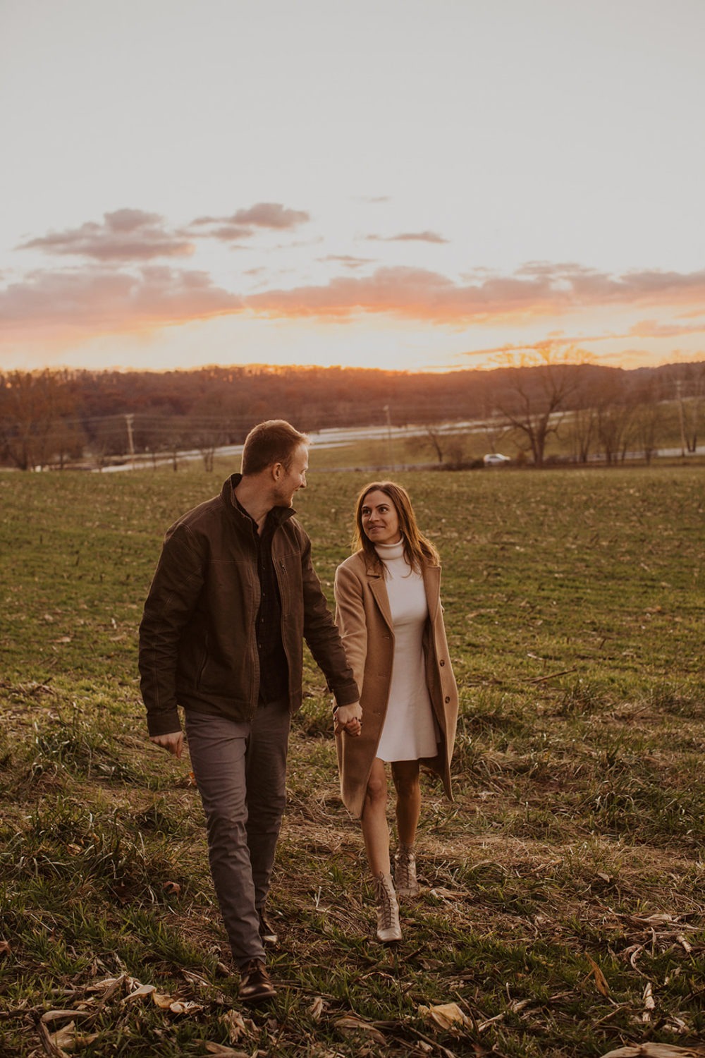 couple walks through field at sunset holding hands