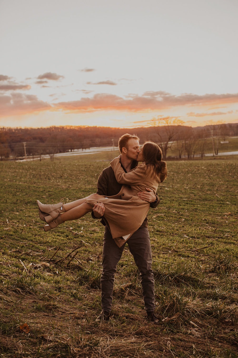 man kisses woman while holding her in field at sunset