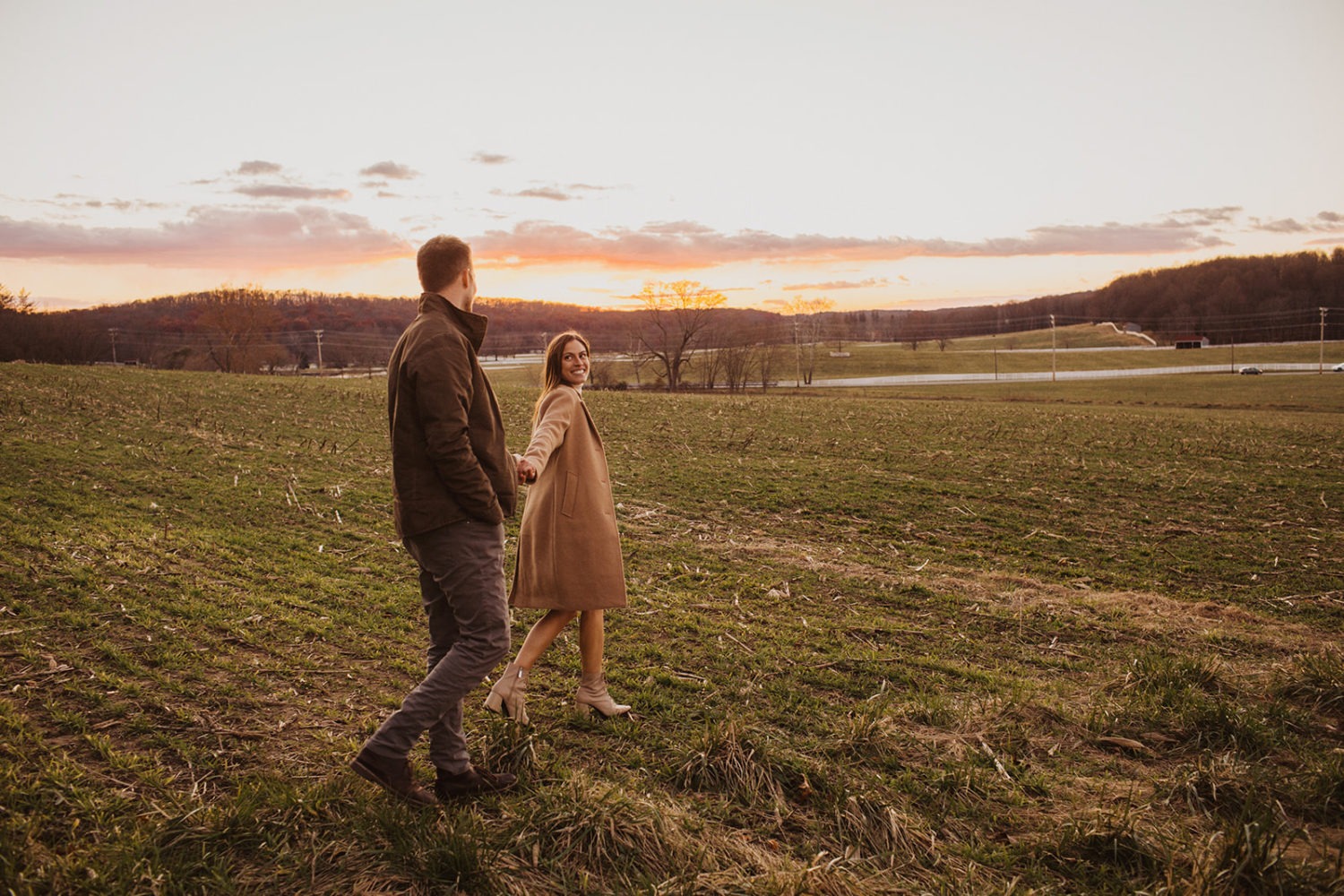 couple walks through field at sunset holding hands