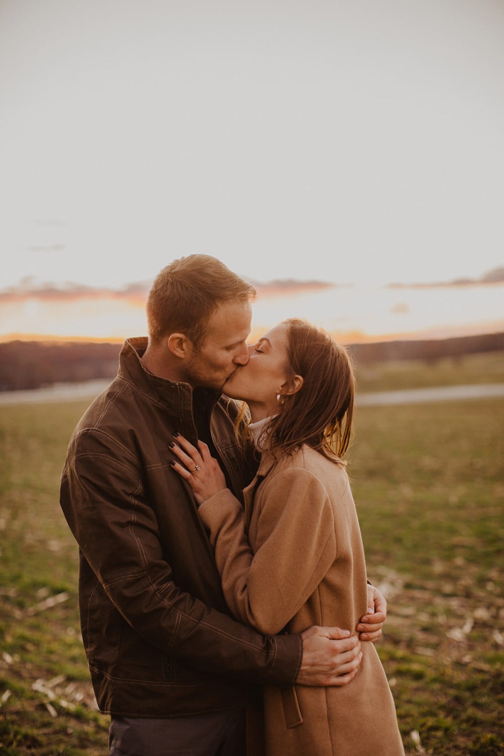 couple kisses standing in field at sunset