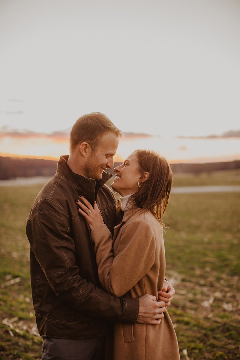 couple almost kisses standing in field at sunset