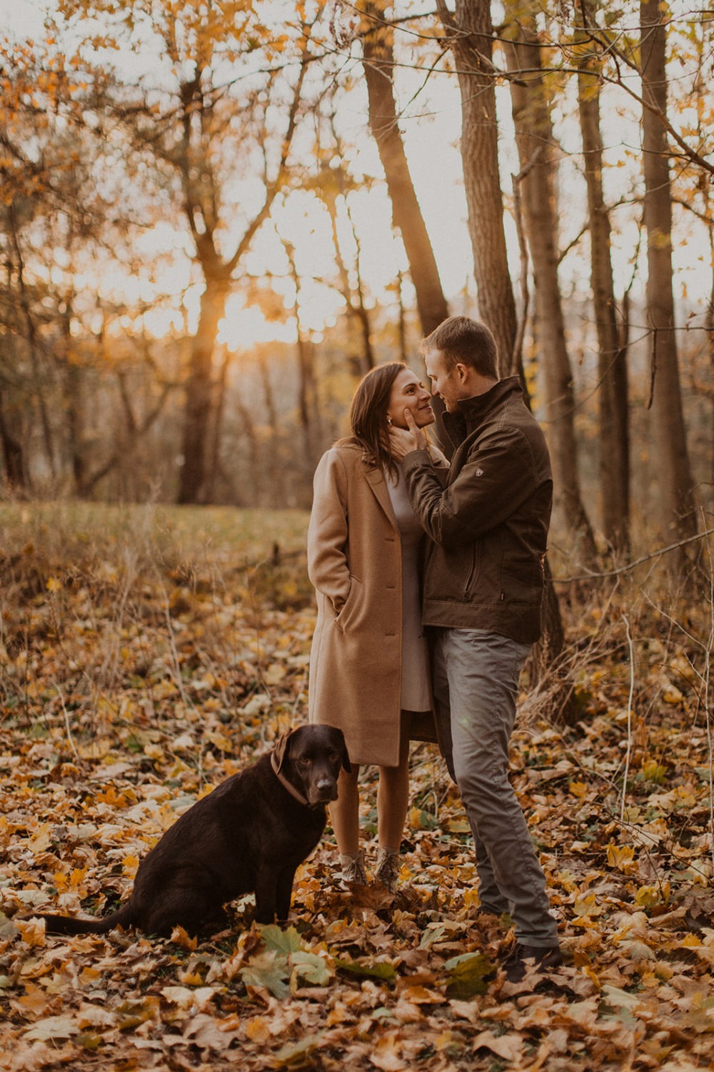 couple embraces surrounded by fall leaves with dog
