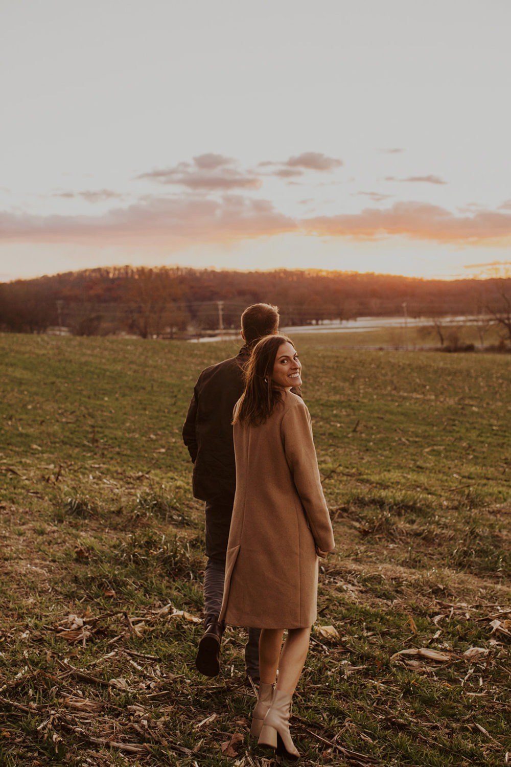 couple walks through field holding hands at sunset